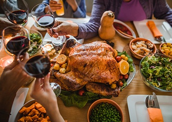 Group of unrecognizable people toasting with wine during Thanksgiving dinner at dining table.