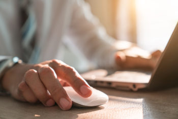hand holding computer mouse with laptop keyboard in the background