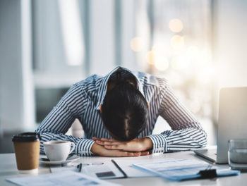 A young businesswoman lies with her head down on a desk in an office.