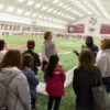 Aggie achieve students at a Texas A&M practice facility talking with football players