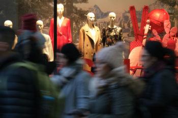 People walk past mannequins in a clothing retailer display window