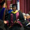 a student holding a diploma shakes hands with faculty as he crosses the stage