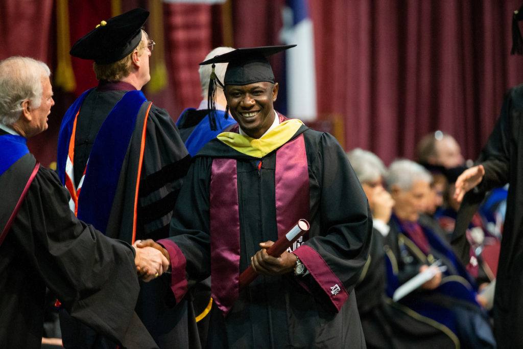 a student holding a diploma shakes hands with faculty as he crosses the stage