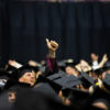 a student standing among graduations in caps and gowns flashes a gig 'em