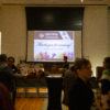 A picture of the event attendees in the Stark Gallery and a project screen with a graphic welcoming attendees