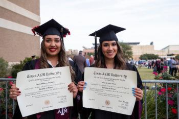 Two graduates in caps and gown holding their degrees