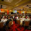people sit at round tables filling a ballroom