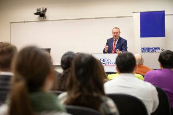 man standing behind a podium speaking to a classroom of students