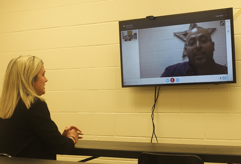 a woman looking at a tv monitor on a wall with a man's face projected