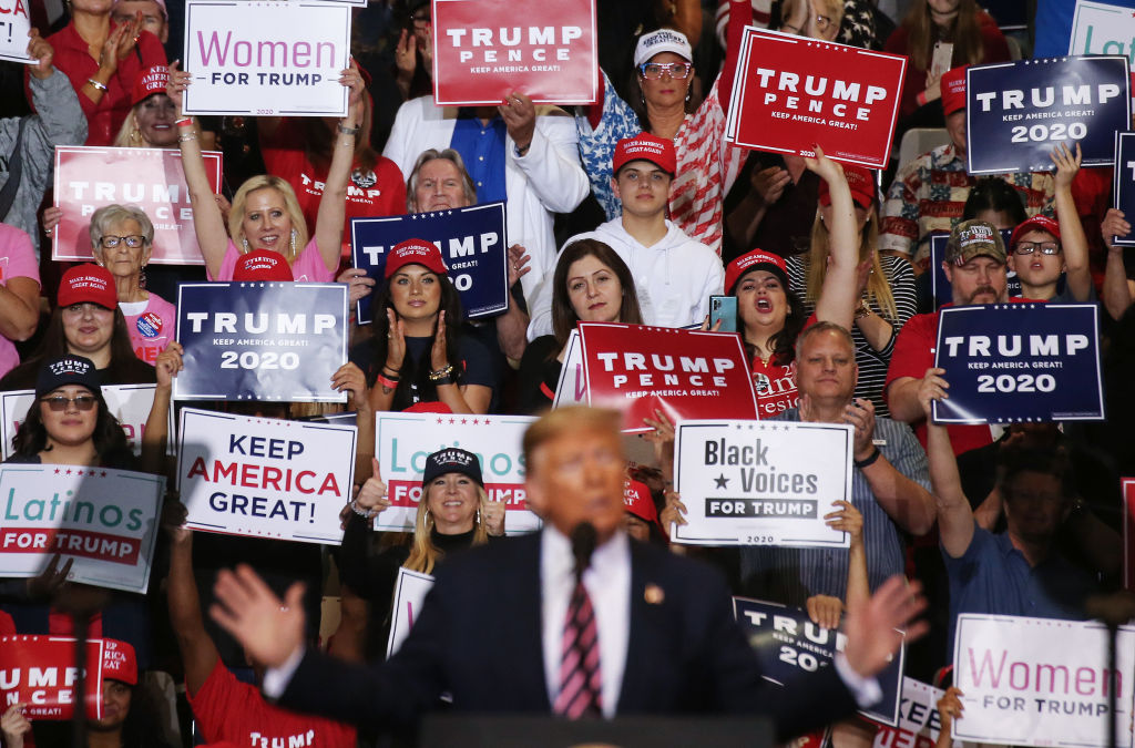 president donald trump speaking with crowd of people in the background holding signs.