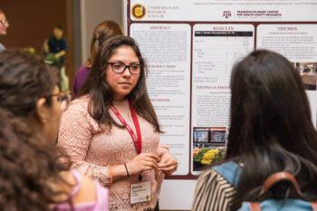 a student standing in front of a poster board presenting research