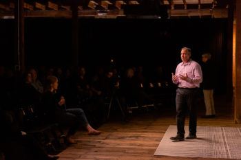 steve martin standing at a front of a room speaking to an audience