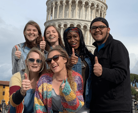Six students pose with thumbs up in front of the Leaning Tower of Pisa