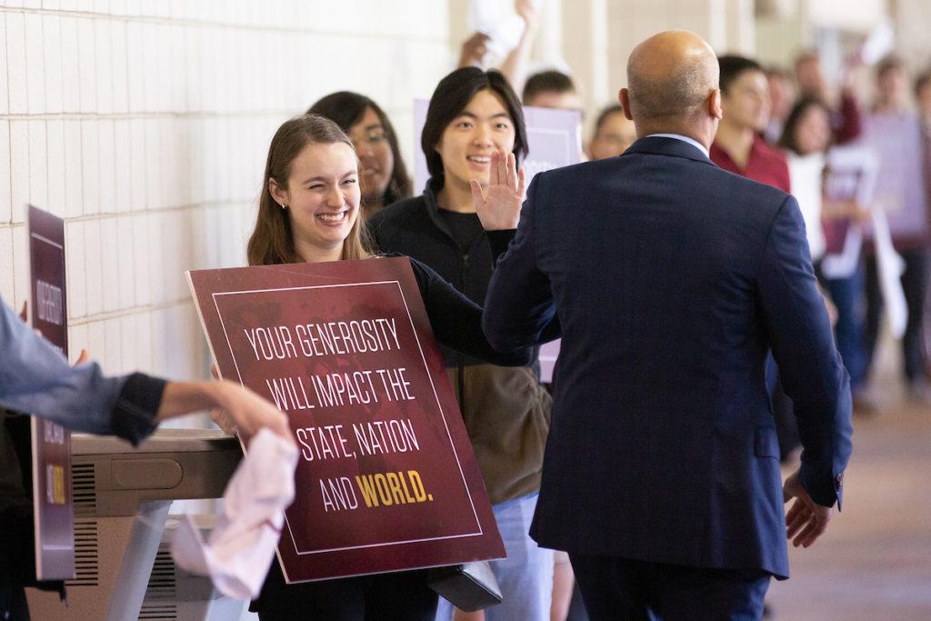 students holding signs cheer as donors walk through the hall of champions