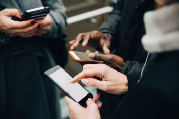 close up of the hands of three people in a circle holding cell phones