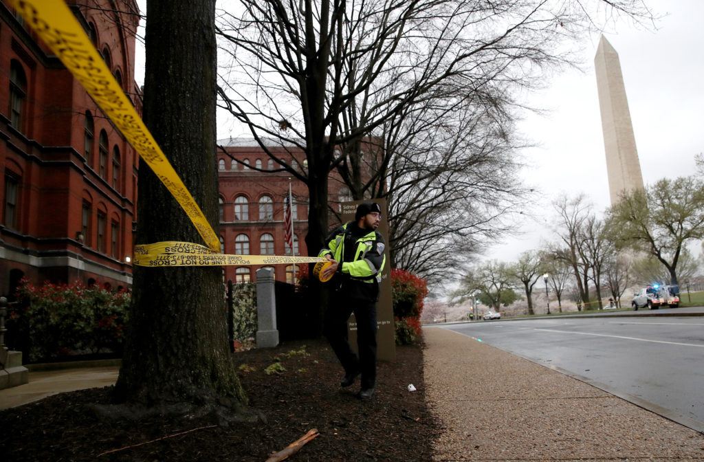 a police officer puts yellow caution tape around a tree in an area with the washington monument in the background
