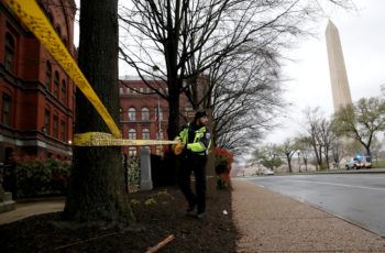 a police officer puts yellow caution tape around a tree in an area with the washington monument in the background