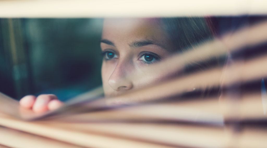 woman at home looking out blinds