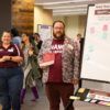 Two librarians standing in front of a white board that has a sign reading Share Your Story, Graffiti Wall, Why are you proud to be an Aggie?