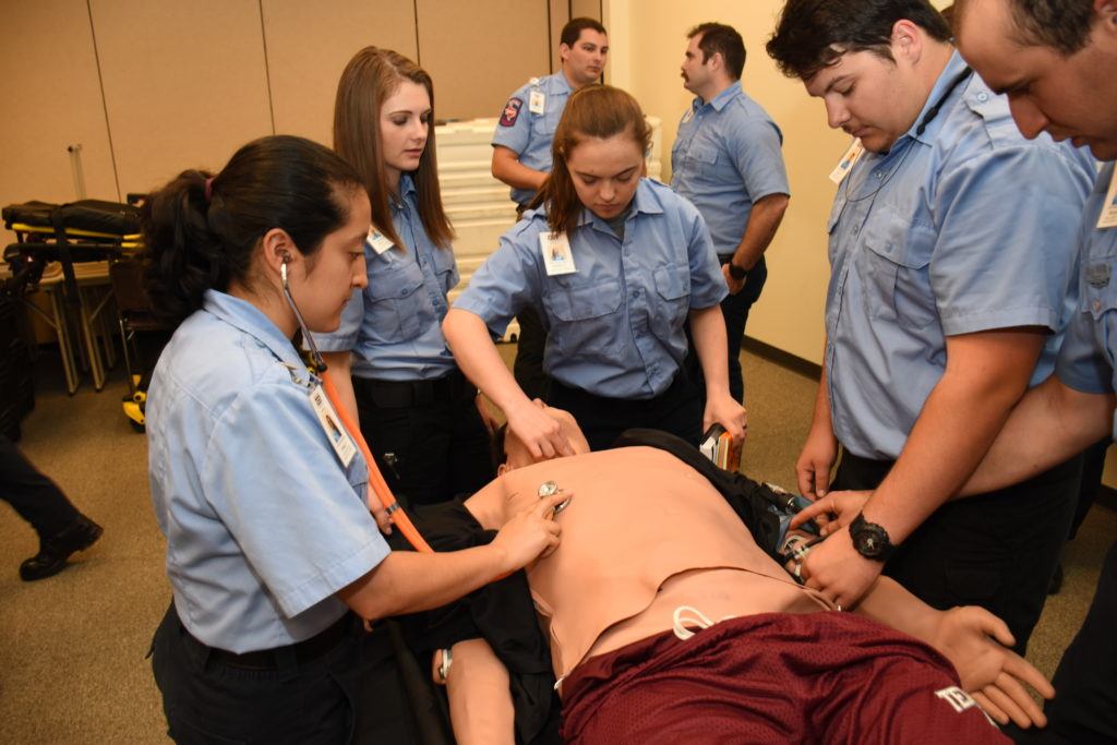 first responders in unison surrounding a manneqwuin, taking its vitals