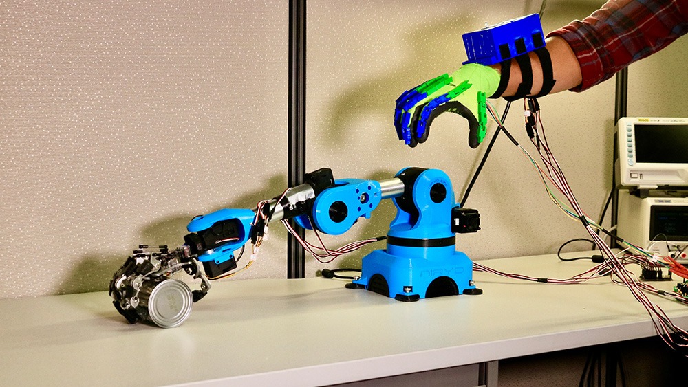 gloved hand with electrodes next to a robotic arm