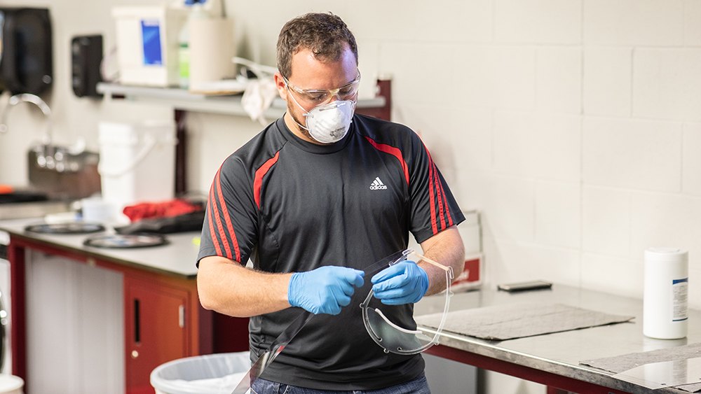 technician in mask and gloves assembles a face shield