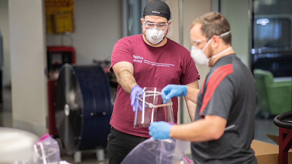 two technicians in lab wearing masks and goggles assembling face shields