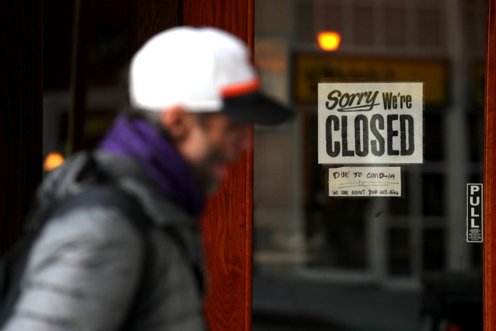 pedestrian walks by a restaurant with a closed sign on the door