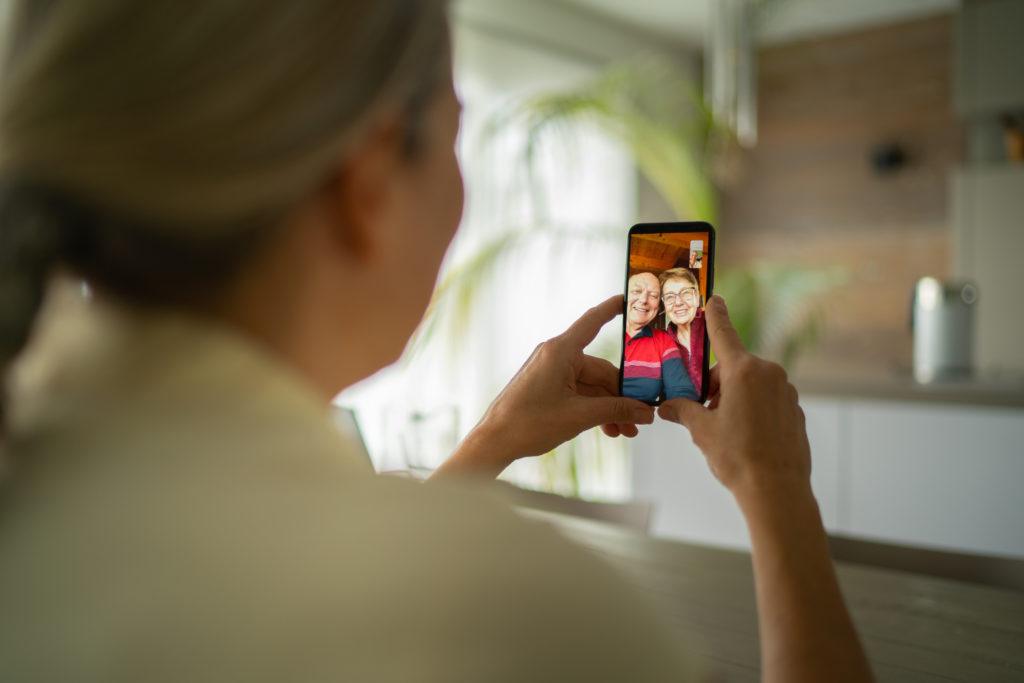 over the shoulder view of adult woman talking with her parents via phone