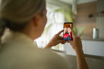 over the shoulder view of adult woman talking with her parents via phone