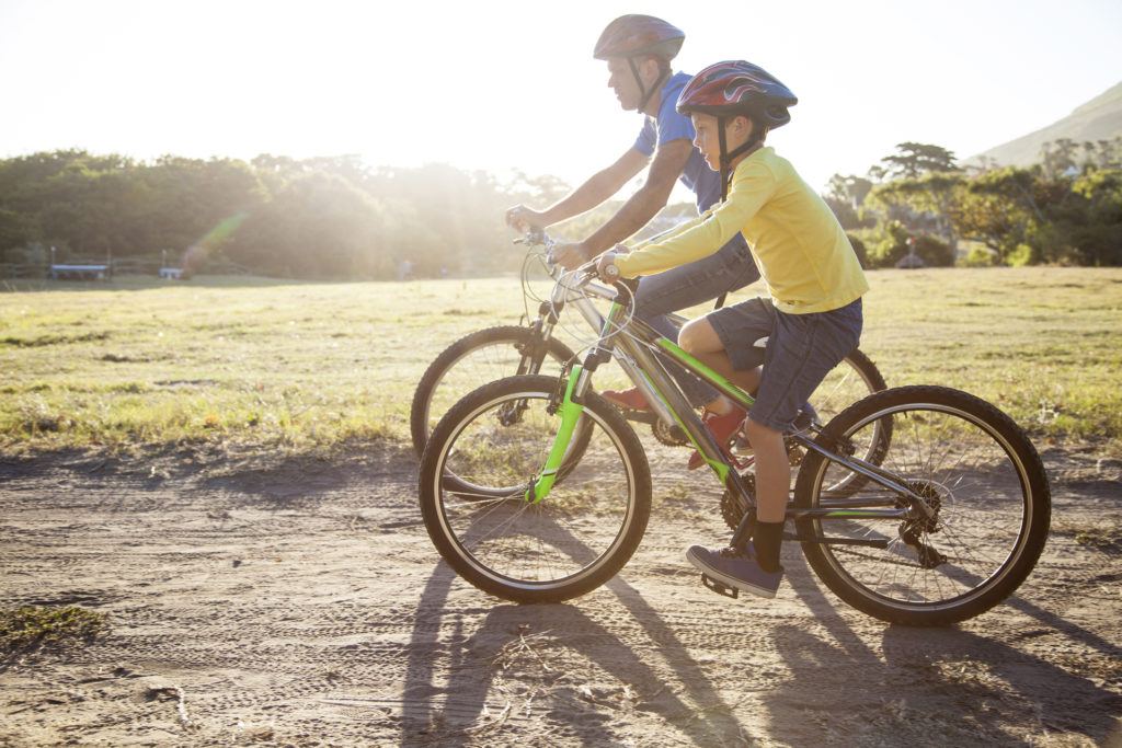 father and son riding bicycles side by side on a dirt path