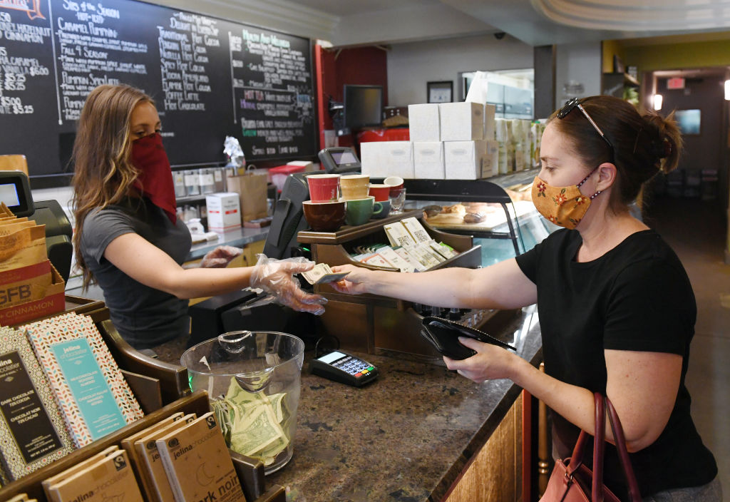 woman wearing face mask behind counter taking money from patron wearing face mask