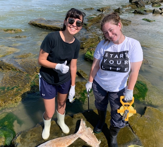 two students standing in water on coast