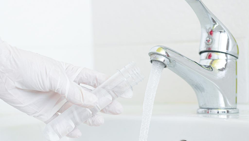 gloved hand holding test tube under running water
