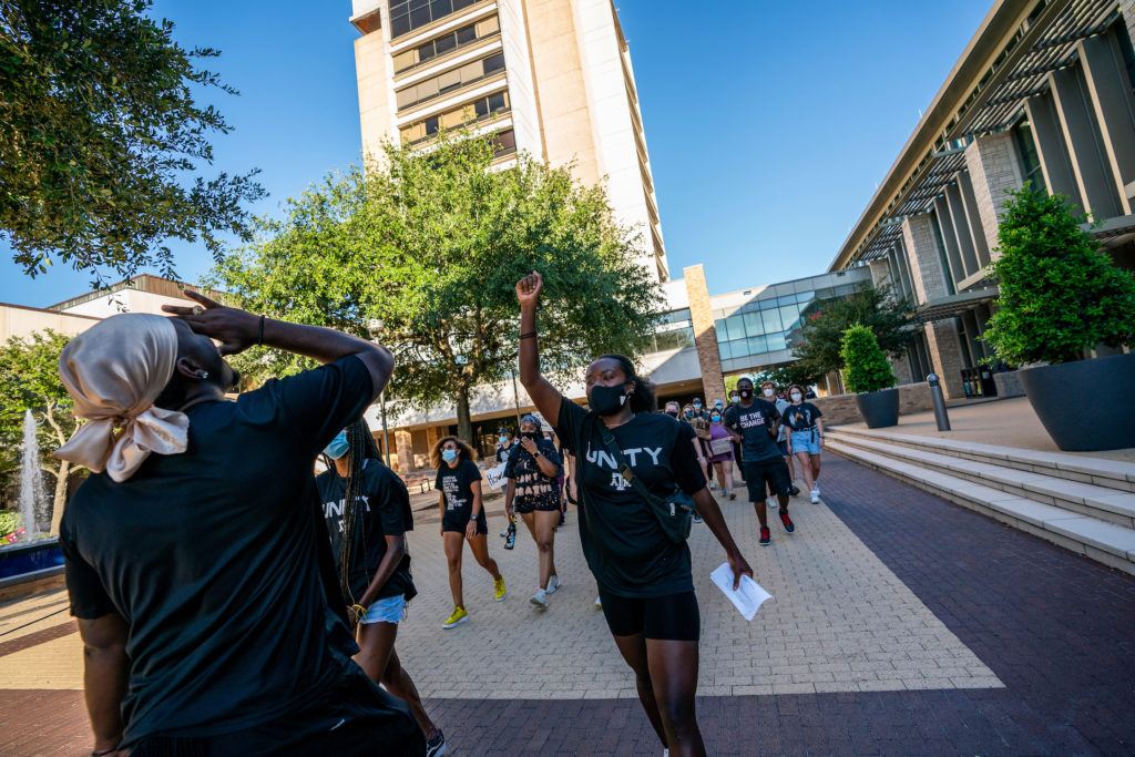 students in foreground raising fists while marching in unity t shirts with rudder tower in background