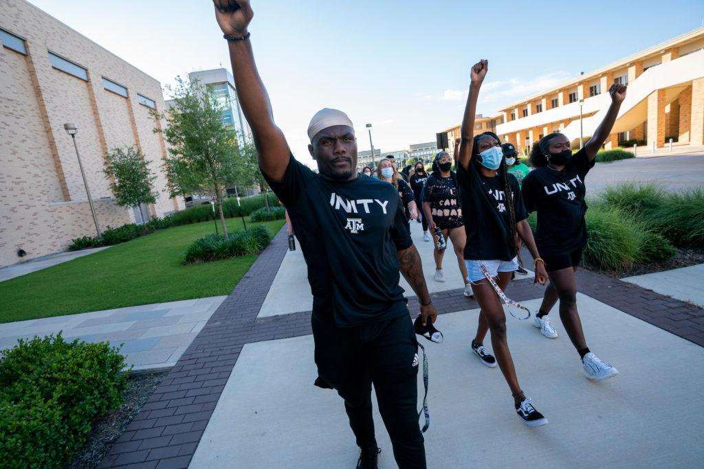 students in foreground raising fists while marching in unity t shirts
