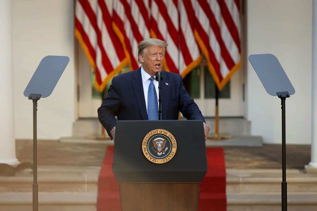 donald trump standin gbehind a podium with american flags in background