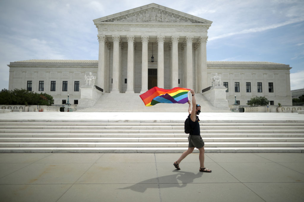 A man holding a Pride Flag walks in front of the U.S. Supreme Court building