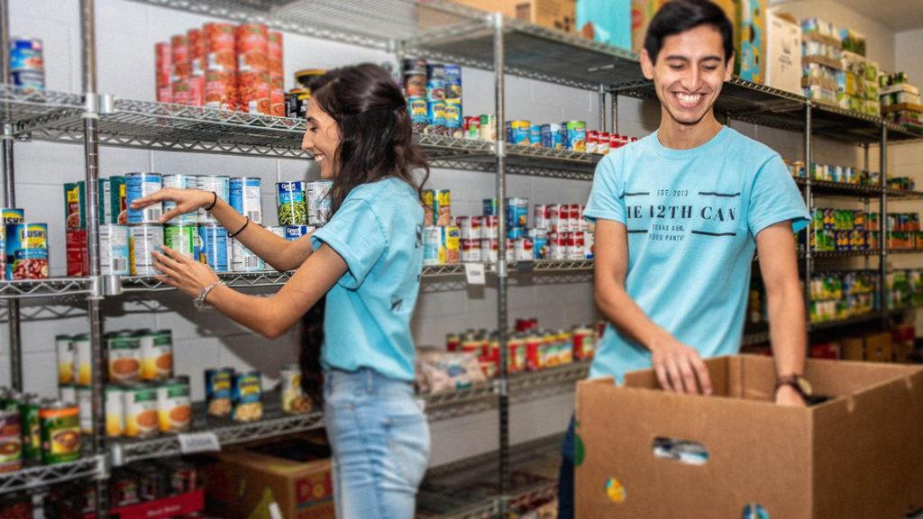 two students wearing blue t shirts standing in food pantry filled with canned goods