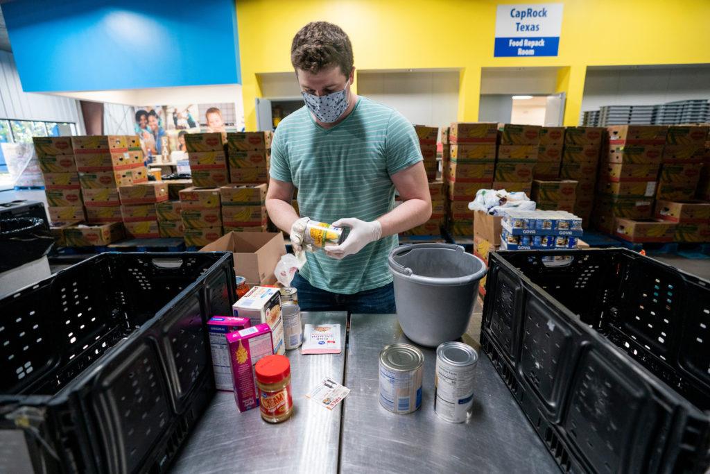a man in a blue t shirt and face mask handles canned goods in a warehouse