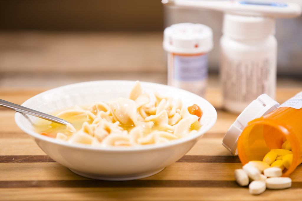 Chicken noodle soup in bowl. Medicines, thermometer. Sick food.