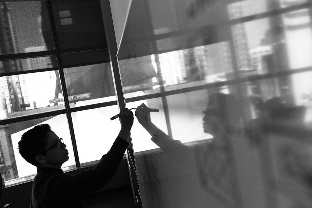 a black and white photo of a man drawing on a whiteboard