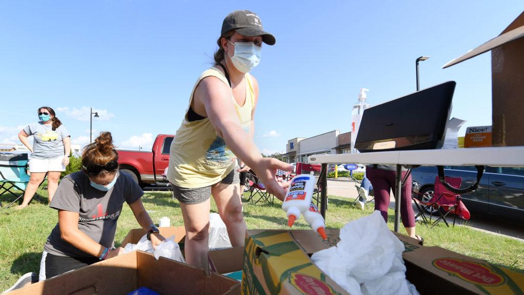 photo of a woman wearing a face mask tossing bottles of glue into a box of school supplies