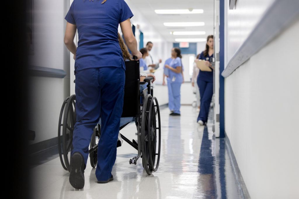 A female nurse pushes an patient in a hospital hallway.
