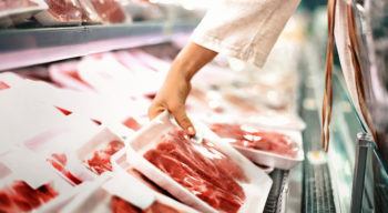 woman's hand picking up package of meat at grocery store