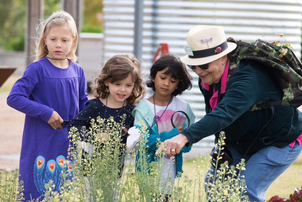 three young girls looking at flowers outside in a garden with a guide