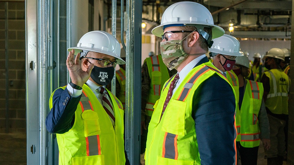 two men in hard hats and yellow safety jackets speak