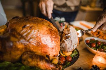 Close up of person carving turkey at dining table.