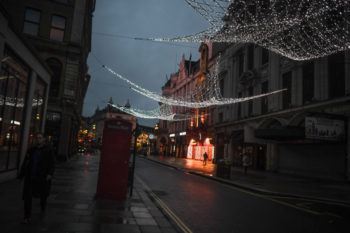 A man walks along an empty street under festive lights in london