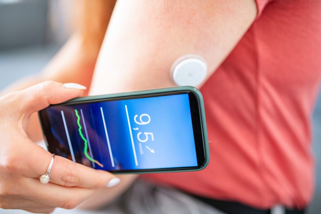close up of young woman with diabetes holding smart phone to swipe sensor on her arm for glucose concentration data.